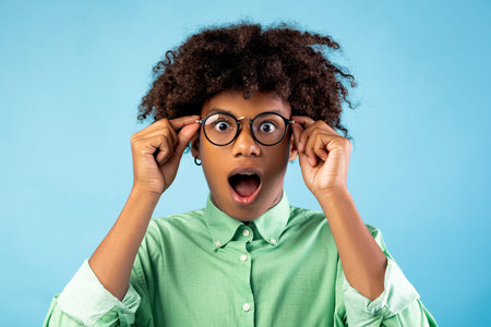 Unbelievable. Shocked black teen guy touching his glasses, opening his mouth, looking at camera on...