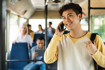 Smiling Asian guy taking bus, talking on cellphoneの写真素材