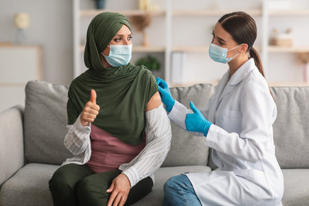 Muslim Lady And Nurse Gesturing Thumbs-Up After Successful Vaccination Indoors