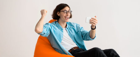 Young Man Celebrates While Watching Something on His Smartphone in a Bright Roomの写真素材