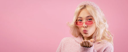 Woman Blowing a Kiss While Wearing Sunglasses and a Cozy Sweater Against a Pink Backgroundの写真素材
