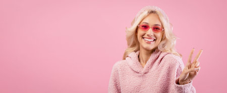 Smiling Woman Giving Peace Sign in Pink Outfit Against Pink Background During Dayの写真素材