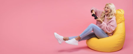 Young Woman Enjoys Video Games While Sitting on a Yellow Bean Bag in a Pink Roomの写真素材