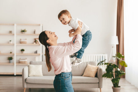 Laughing young mother playing with cute toddler son, holding funny kid pretending flying, having fun...