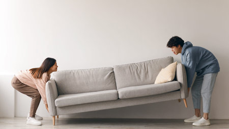 Couple Moves a Sofa Across a Room During Home Rearrangement in a Modern Living Spaceの写真素材