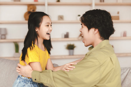 Happy asian millennial man and teen daughter look at each other with open mouths, have funの写真素材