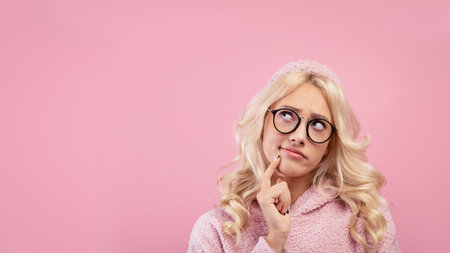 Woman Thinking While Wearing Glasses Against a Pink Background Showing Curiosity and Wonderの写真素材