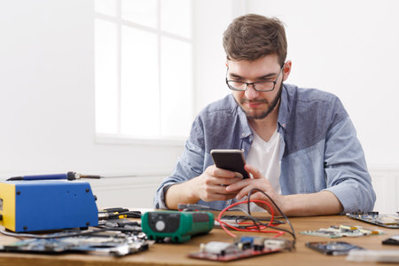 Young Man Works With Tools and Checks Phone in a Workshopの写真素材