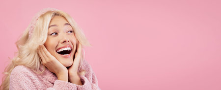 Smiling Woman in Pink Sweater Looks Excited Against a Pink Background at a Studio Settingの写真素材