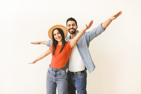 Young couple in love pretending airplane flight, spreading hands like wings, having fun while posing over light studio wallの写真素材