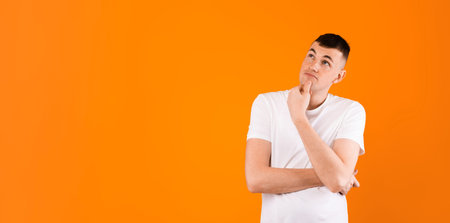 Pensive caucasian man looking aside at copy space and touching chin, thinking about interesting...