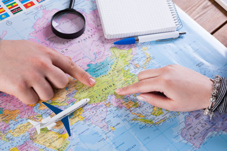 Hands Pointing at a Map of China With a Model Airplane and Writing Tools Nearby