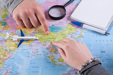 People Pointing at a Map of China With a Model Airplane Nearby and Writing Materials Set Out