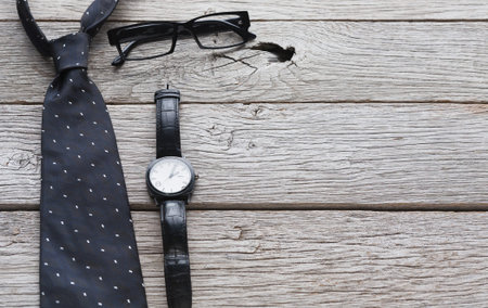 Dark Tie, Black Watch, and Glasses Placed on Wooden Surface and Ready for Use at a Formal Eventの写真素材