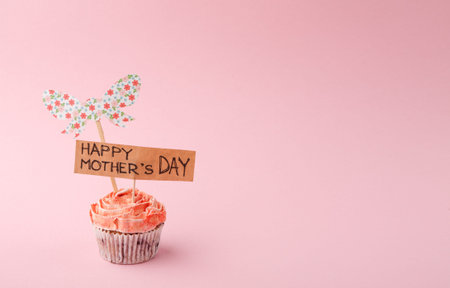 Cupcake With Happy Mothers Day Sign and Floral Bow on Pink Background for Celebration