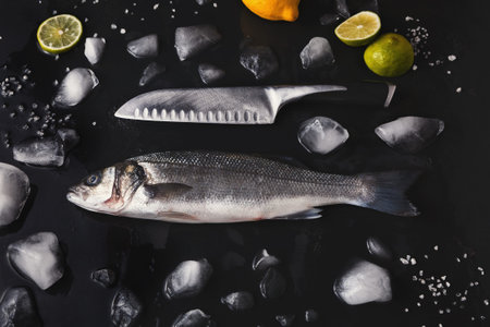 Fresh Fish and Knife on a Black Surface With Ice and Citrus Fruits During a Food Preparation Sceneの写真素材