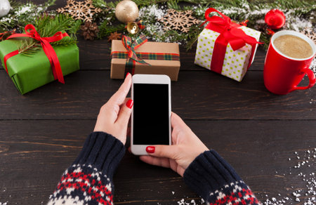 Person Holding Smartphone Next to Wrapped Gifts and Coffee Cup During Winter Season
