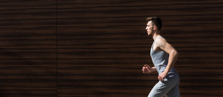 Young Man Runs Along a Brown Wooden Wall During Daytime Exercise Session in Urban Areaの写真素材
