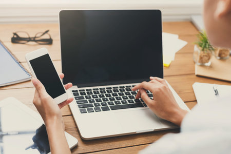 Person Using Laptop and Smartphone on a Wooden Desk During the Day
