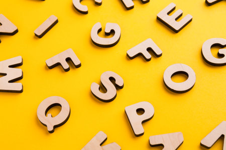 Wooden Letters Scattered on a Bright Yellow Surface in Various Orientations and Sizesの写真素材