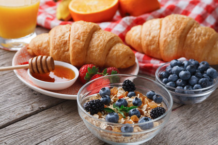 Breakfast Spread Featuring Croissants, Yogurt, Fruit, and Honey on a Wooden Tableの写真素材