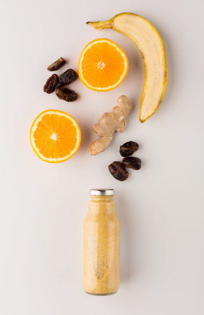Fresh Fruit and Healthy Drink Layout With Banana, Orange, Ginger, and Dates on a Simple Surfaceの写真素材
