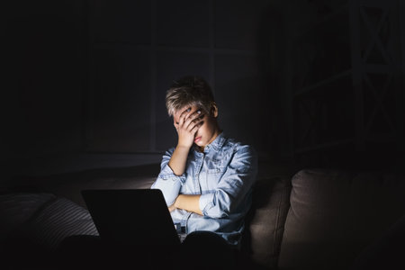 Young Person Works on Laptop While Feeling Tired During Nighttime Hours in a Dimly Lit Room