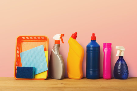 Collection of Cleaning Supplies Arranged on a Wooden Table Against a Pink Background