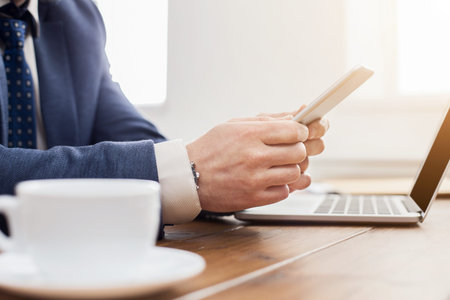 Business Professional Uses Smartphone While Working on Laptop at Desk