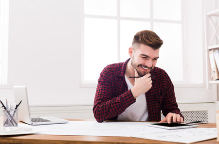 Man Working on a Digital Tablet While Sitting at a Desk in a Bright Room