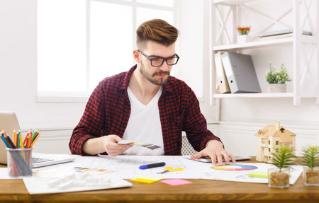 Young Man Works on Design Project at Desk During Daytime in Home Office Environment