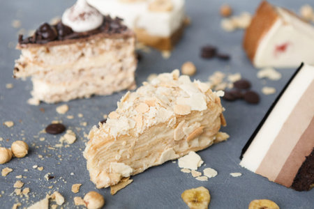 Collection of Various Dessert Slices Arranged on a Gray Surface With Nuts and Chocolate Pieces