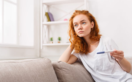Woman Sitting on Couch Holding Pregnancy Test at Home in Afternoon