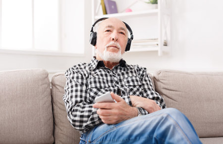 Elderly Man Listens to Music on Couch in Living Room During Afternoon