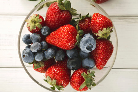 Collection of Fresh Strawberries and Blueberries in a Clear Bowl on a Wooden Table