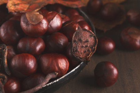 Collection of Chestnuts in a Bowl With Dried Leaves on a Wooden Surface During Autumn