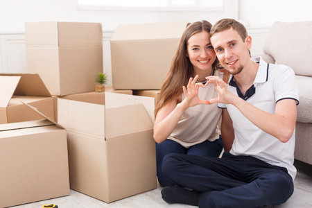 Couple Makes Heart Shape With Hands Among Moving Boxes in Their New Home