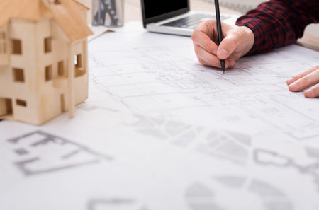 Architect Designs Building Plans While Working at a Desk With a Model House and Laptop