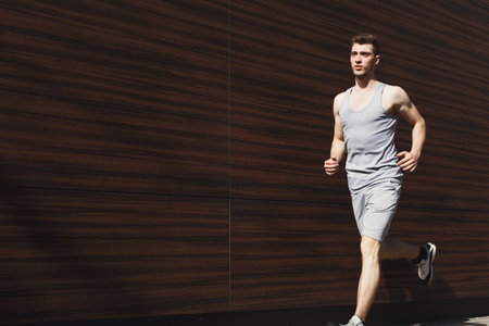 Young Man Runs in Active Wear Against Wooden Wall on Sunny Day in Urban Setting