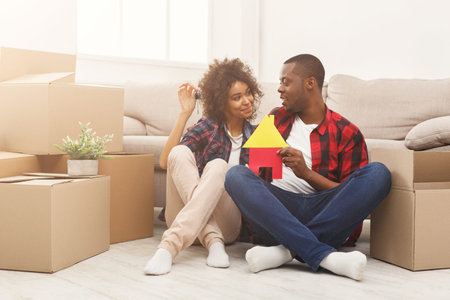 Couple Sits on Floor Among Boxes While Holding a Model of a House in New Home Setup
