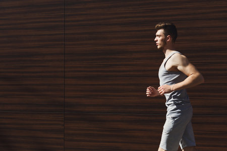 Man Jogs on a Sunny Day Next to a Wooden Wall in a Casual Running Outfit
