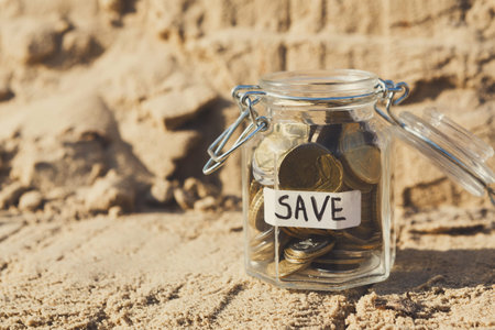Money Jar Collects Coins on Sandy Beach During Sunny Day