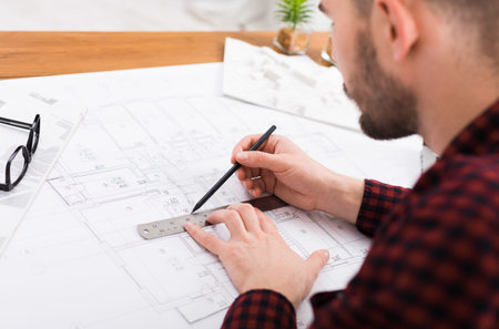Architect Works on Building Plans With Pencil and Ruler on a Table Indoors