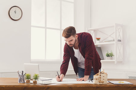 Man Working on Architectural Plans in Modern Office With Plants and Model House