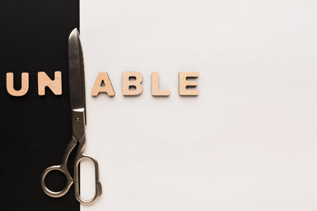 Scissors Placed Next to Wooden Letters Spelling Unable on Black and White Backgroundの写真素材