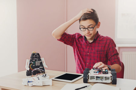 Boy Works on Robot Project With Tablet and Robotics Kit in Classroom During Afternoon