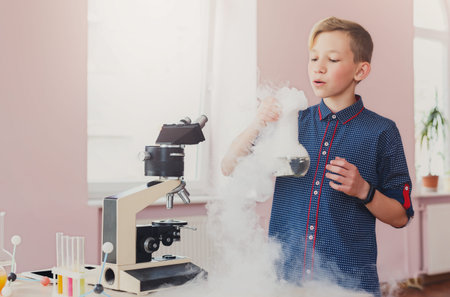 Boy Conducts Science Experiment With Fog and Microscope in Classroom Settingの写真素材