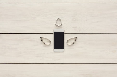Collection of a Mobile Phone With Wings and Bell on Wooden Surface in Creative Designの写真素材