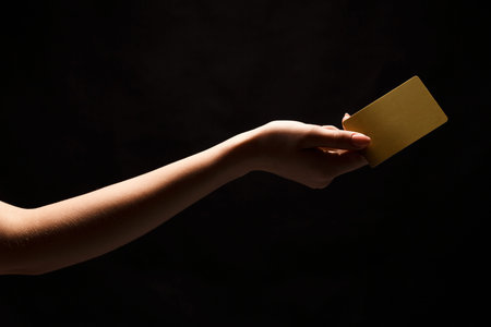 Hand Reaching out to Offer a Card Against a Dark Background in a Simple Setupの写真素材