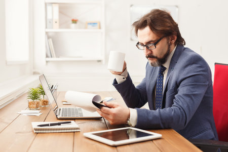 Man Working in an Office With Coffee, Laptop, and Documents on Desk at Daytime